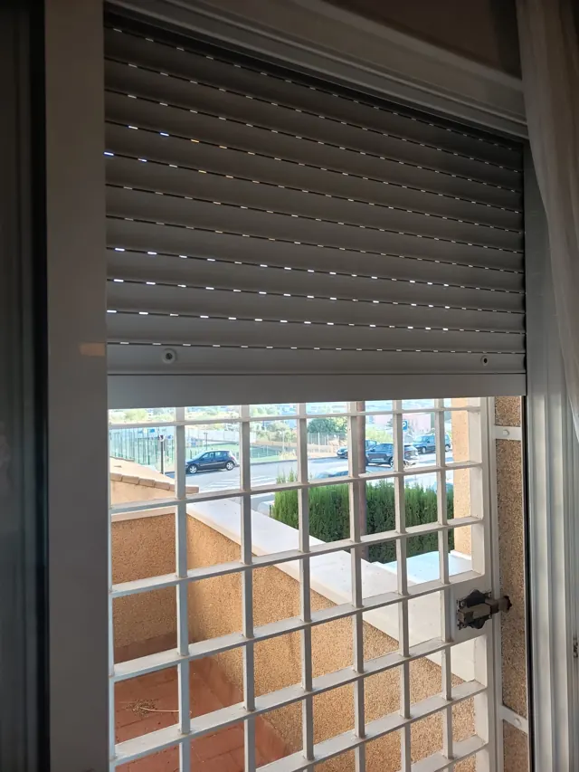 Persiana de aluminio reparada sobre una ventana con reja